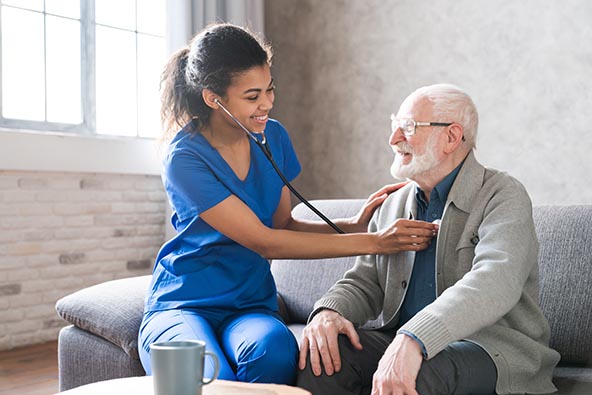 Young African American woman checking vitals of older white man wearing glasses and gray cardigan 